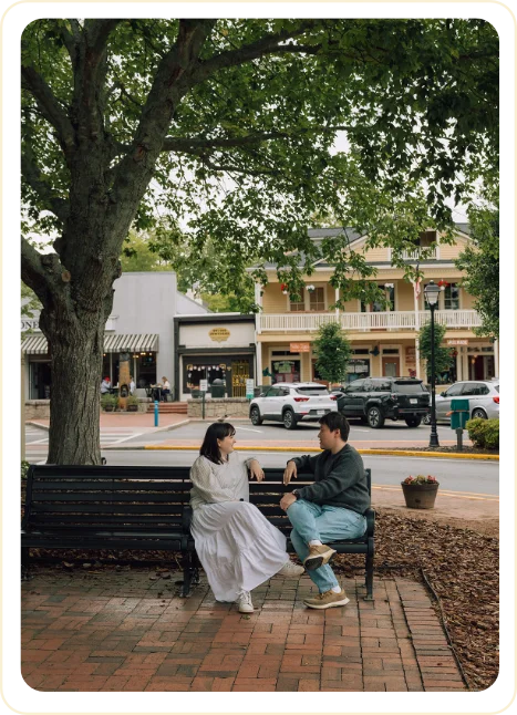 Sarah and Ji chatting on a bench under a large tree in downtown Dahlonega
