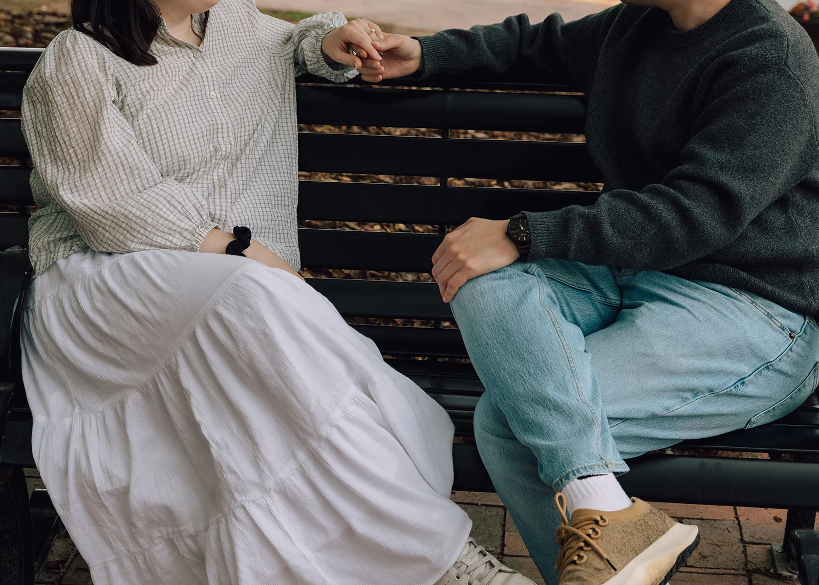 Sarah and Ji sitting together on a park bench, holding hands