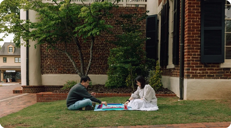 Sarah and Ji playing a board game on a picnic blanket on the lawn