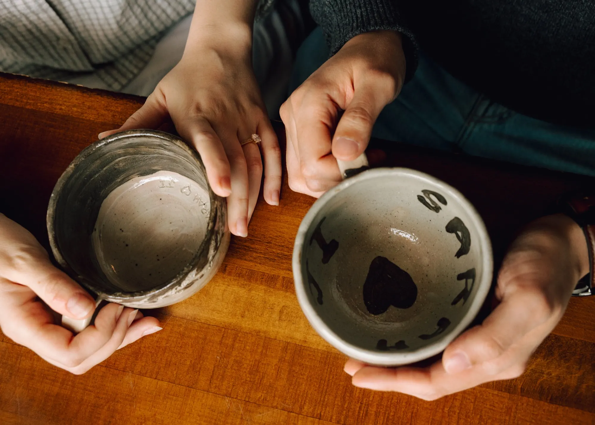 Sarah and Ji holding handmade mugs painted with each other's names and a heart